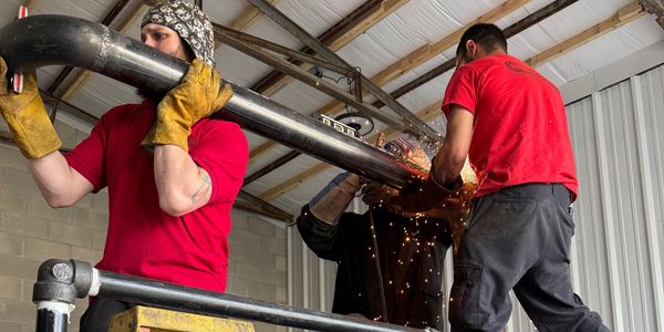 Three men working on a large metal pipe indoors.