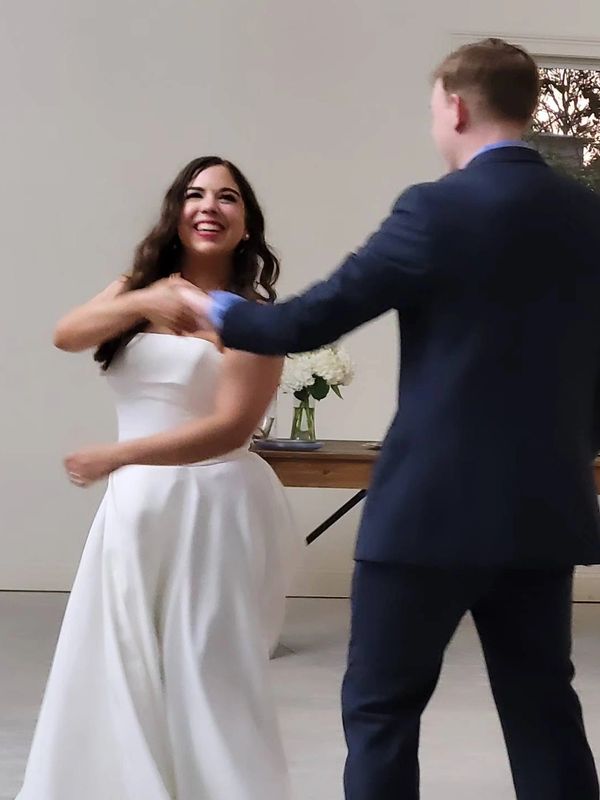A joyful bride in a white dress dancing with a groom in a navy suit.