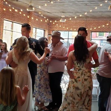 Couples dancing at a lively indoor wedding reception with string lights.