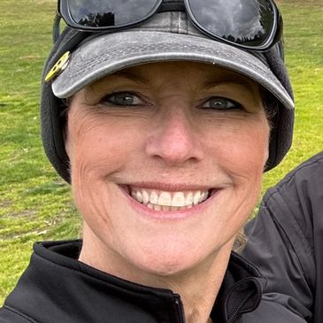 Smiling woman outdoors wearing a cap and sunglasses on her head.