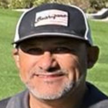 Smiling man wearing a cap outdoors on a sunny day.