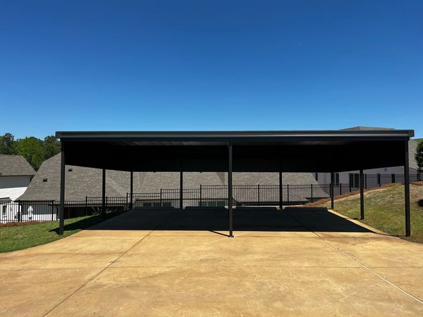 Empty outdoor parking area with metal carport under clear blue sky.