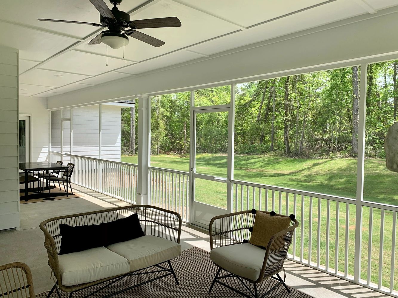 Bright screened porch with modern outdoor furniture and ceiling fan overlooking green yard.