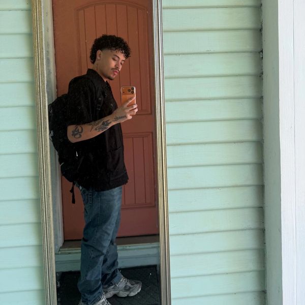 Young man taking a mirror selfie outside with a backpack.
