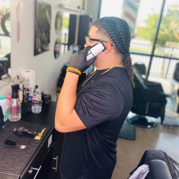 Barber with braids talking on phone in barbershop.