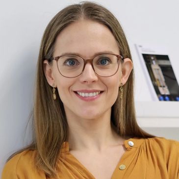 Smiling woman with glasses and long hair in mustard top.
