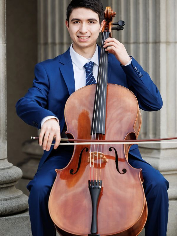 Young man in blue suit playing a cello outdoors.