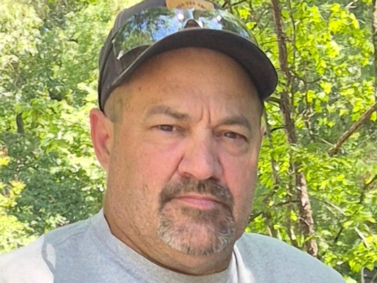 Man with a cap and sunglasses outdoors in a forest.