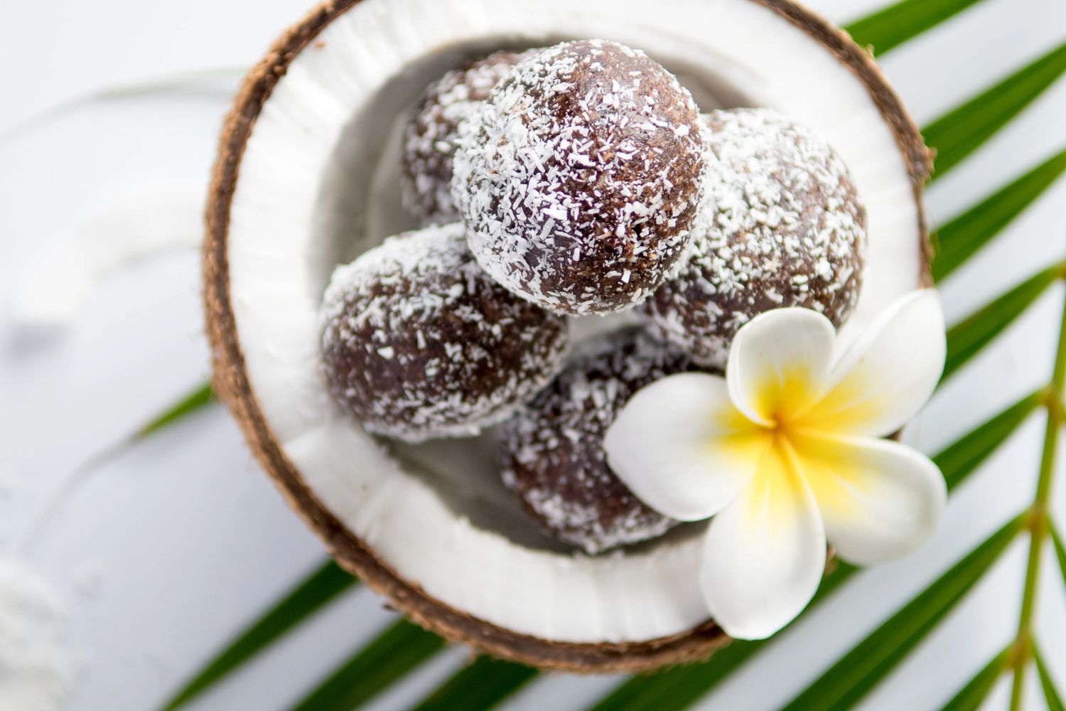 Chocolate coconut balls in a coconut shell with a white and yellow flower.