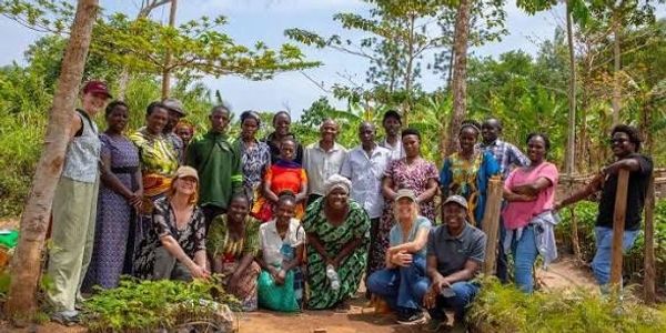 A diverse group gathers outdoors among young plants in a natural setting.