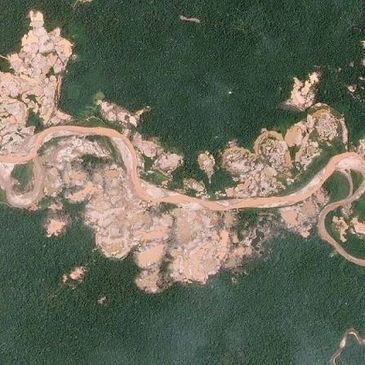 A winding dirt road cuts through dense green forest and rocky terrain.