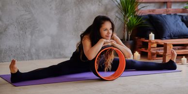Woman stretching on a yoga mat using a yoga wheel for support.