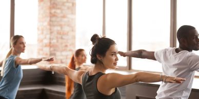 Group of people doing yoga stretches in a bright studio.
