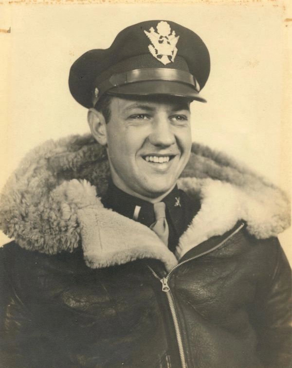 Smiling World War II pilot in leather jacket and military cap.