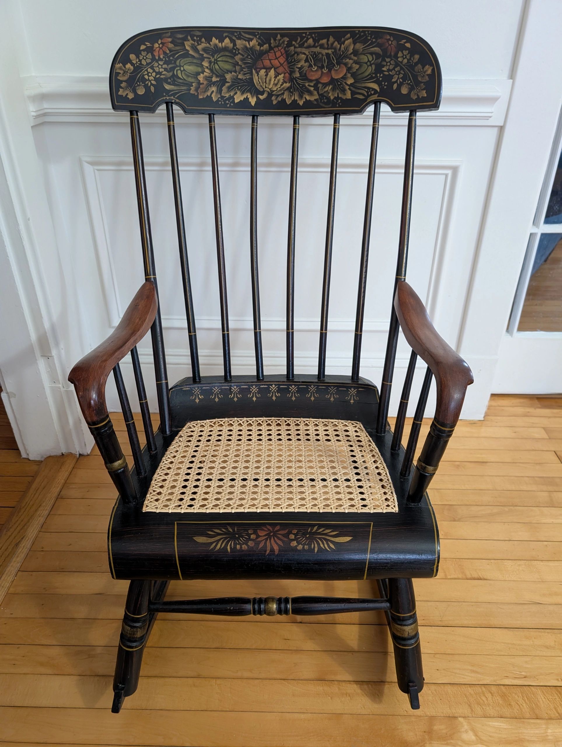 Decorative black wooden rocking chair with floral design and woven seat.