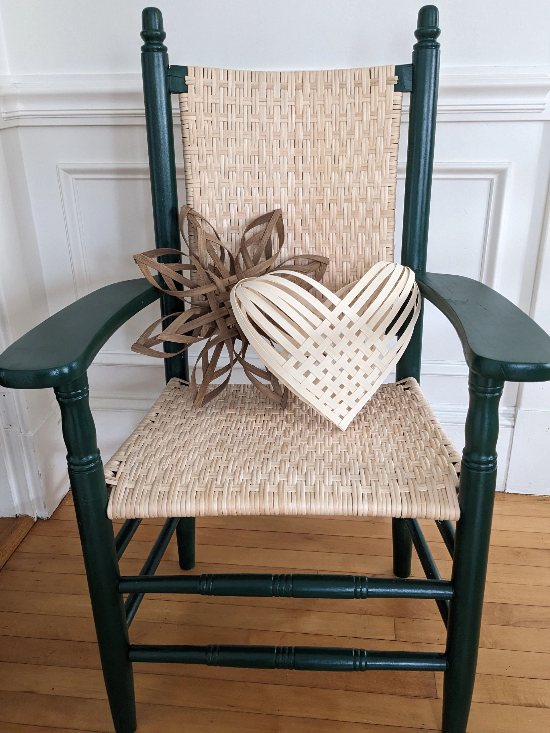 Woven heart and flower decor on a green wooden chair with woven reed seat and back.