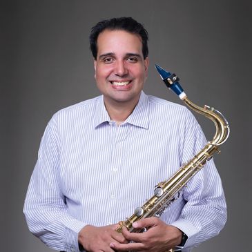 Smiling man holding a saxophone against a plain background.