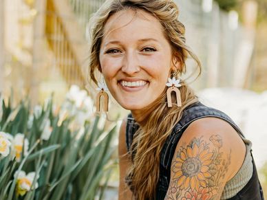 Smiling woman with sunflower tattoo and unique earrings.