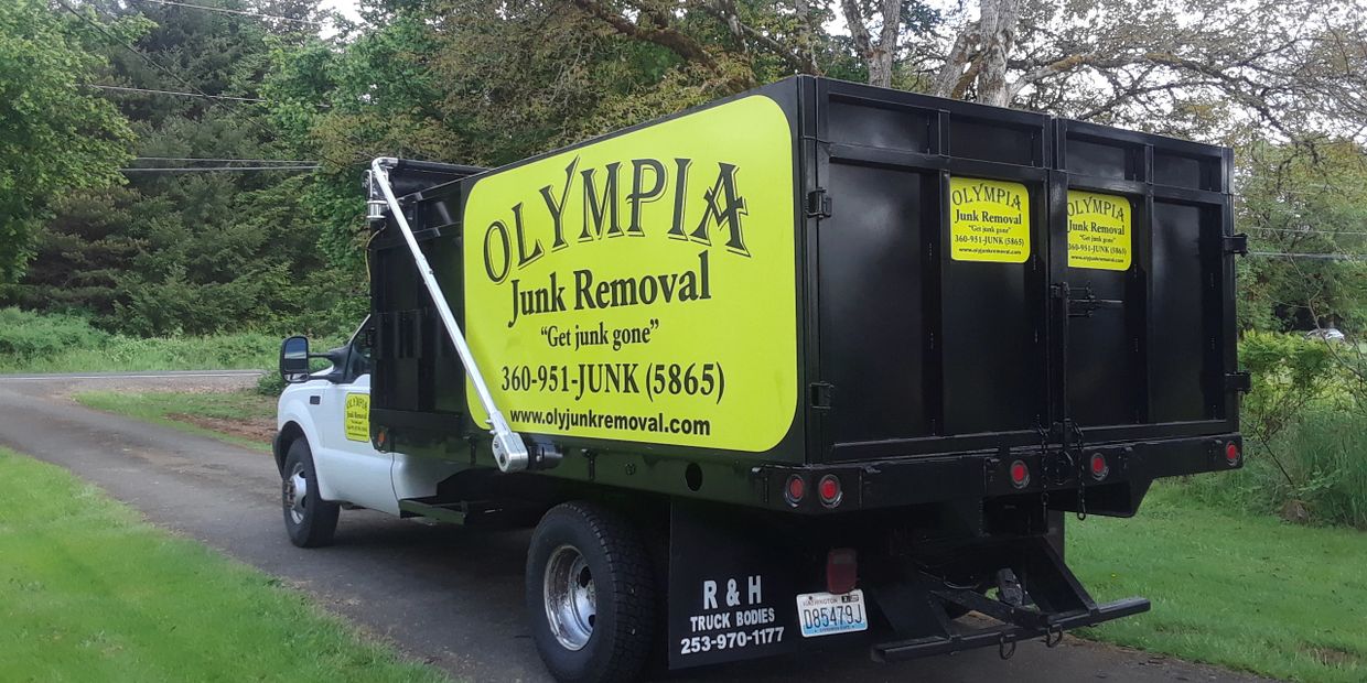 A black and white truck with bright yellow signage for Olympia Junk Removal parked on a driveway.