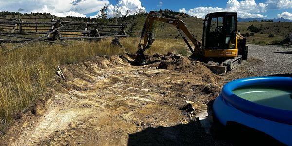 Excavator digging for a retaining wall to expand an existing Gravel Driveway.