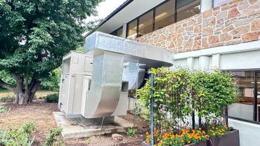 Outdoor HVAC unit beside a stone building.