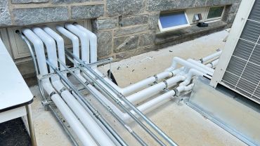 White pipes and conduits on a concrete surface near a stone wall.