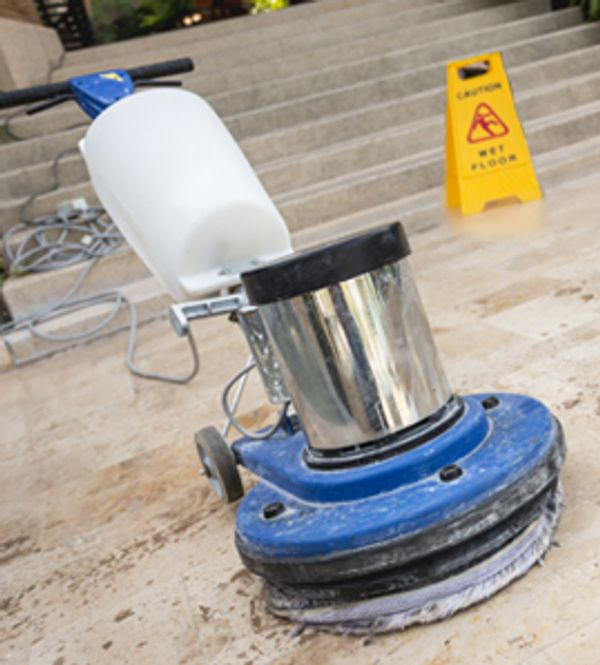 Floor cleaning machine on a wet floor with caution sign.