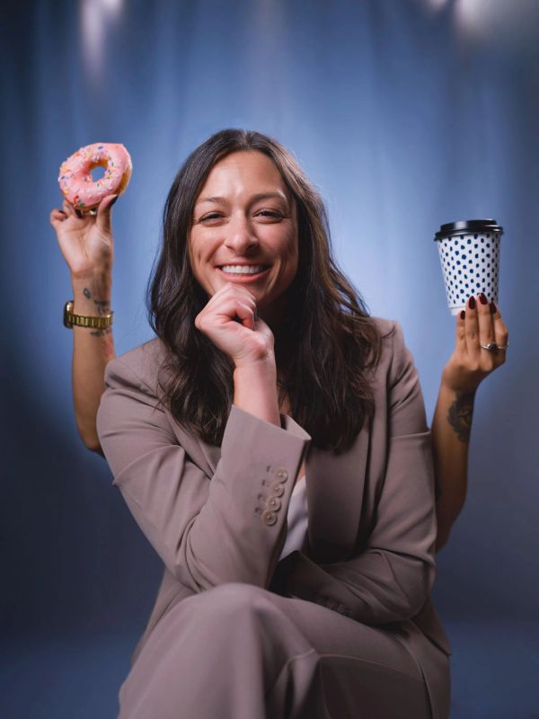 Woman smiling with hands holding a donut and a coffee cup.