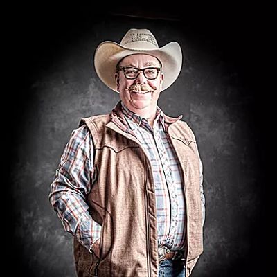 Man in a cowboy hat smiling with a black background