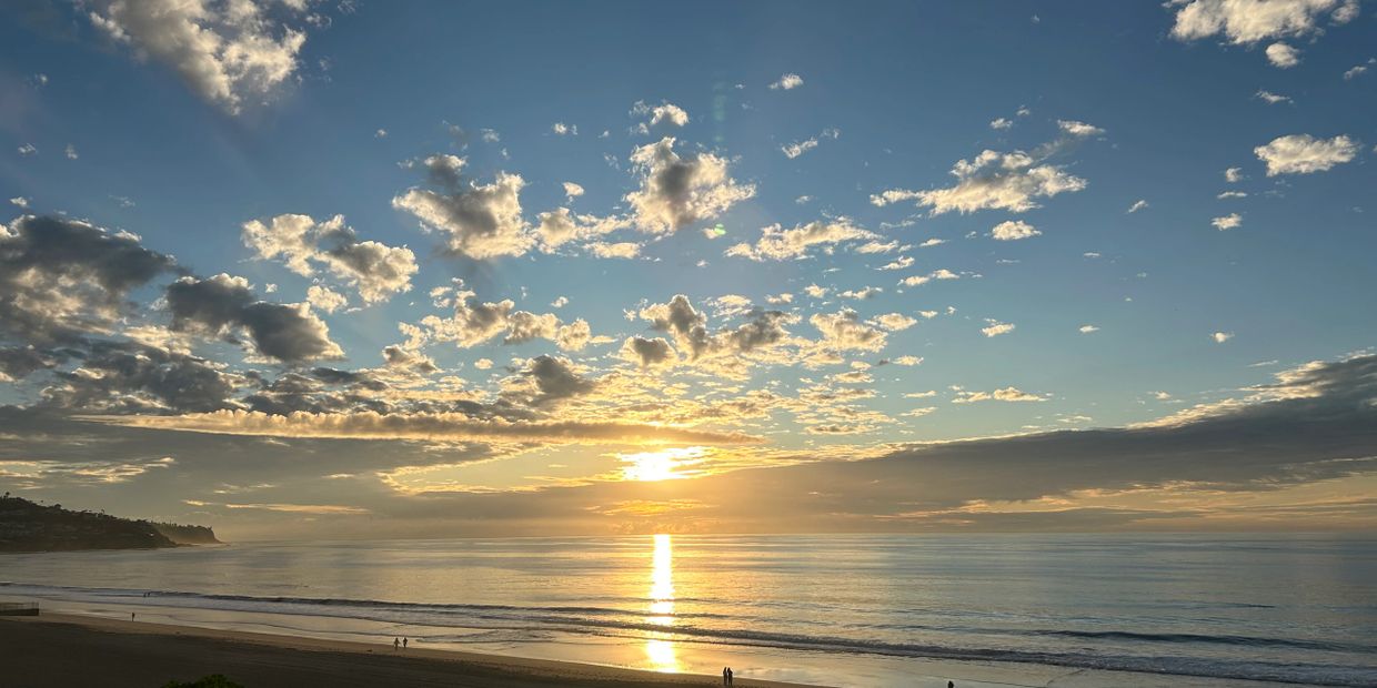 Sunset over a calm beach with scattered clouds and gentle waves.