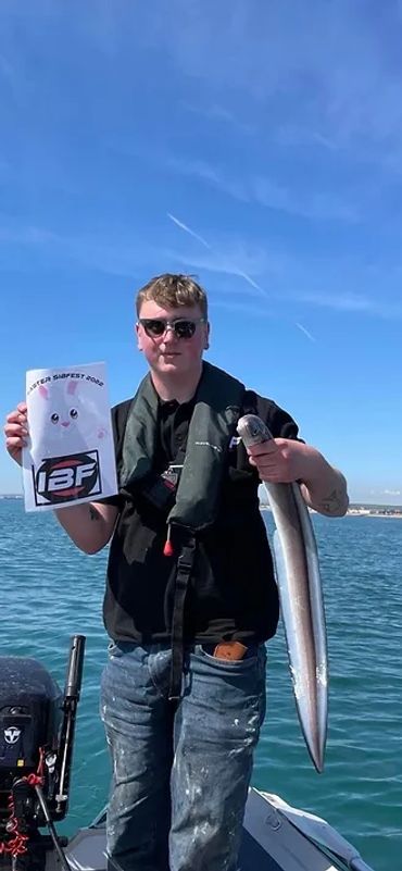 Man holding a long fish and a sign on a boat under clear blue sky.