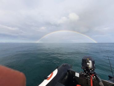 Rainbow over calm sea seen from a boat with fishing gear.