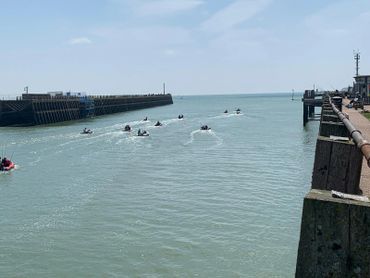 Several jet skis moving away from a harbor into open water on a sunny day.