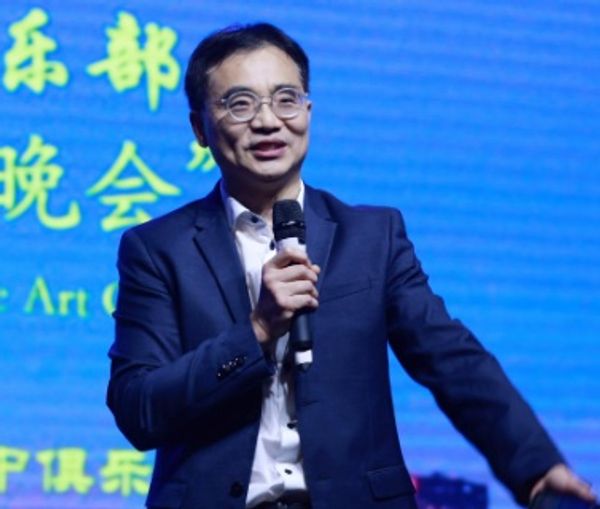 Man in suit speaking on microphone against blue backdrop with Chinese text.