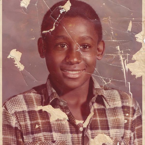 Young boy in a plaid shirt with a smiling face and a worn, torn photo.