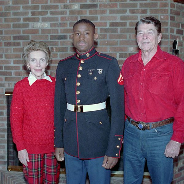 A young Marine stands between an elderly couple in a cozy room.