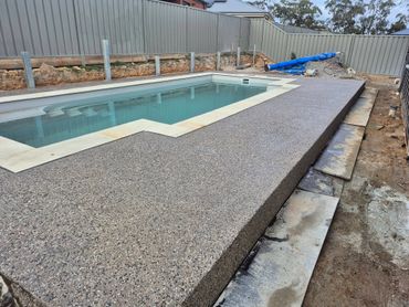 Newly constructed backyard pool with textured concrete decking and metal fencing.