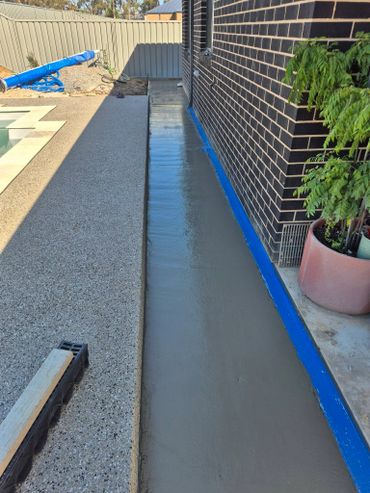 Freshly poured concrete walkway along a brick house wall.