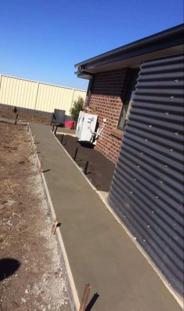 Newly poured concrete walkway beside a brick house under clear blue sky.