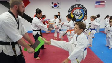 Children and instructors practicing martial arts in a dojo.