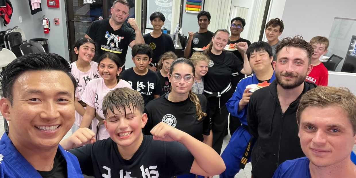 Group of smiling martial arts students and instructors in uniforms posing for a photo indoors.