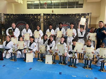 Group photo of martial artists with certificates and trophies.