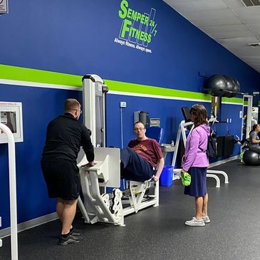 People working out and socializing in a well-lit gym with blue walls.