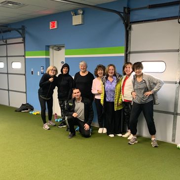 Group of seven people posing in a spacious indoor gym with green flooring and blue walls.