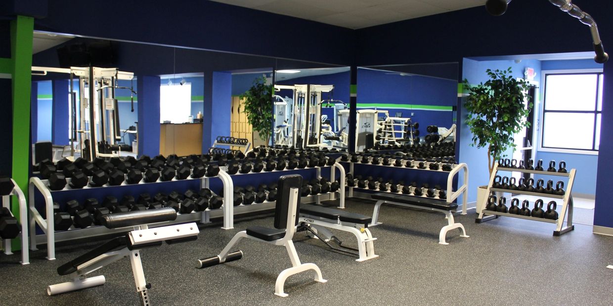 Bright gym corner with dumbbells, kettlebells, benches, and mirrors.