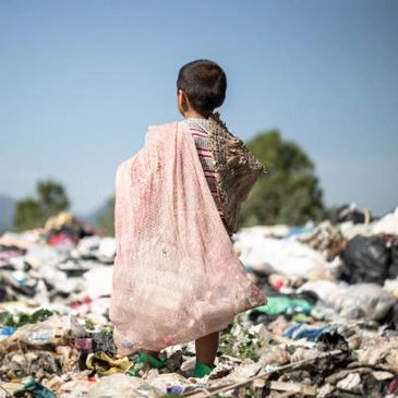 Child carrying a large sack in a landfill site.