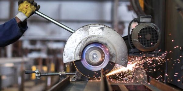 Worker cutting metal with grinding wheel emitting sparks.