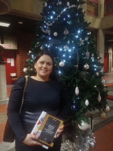Woman smiling near a decorated Christmas tree holding books.