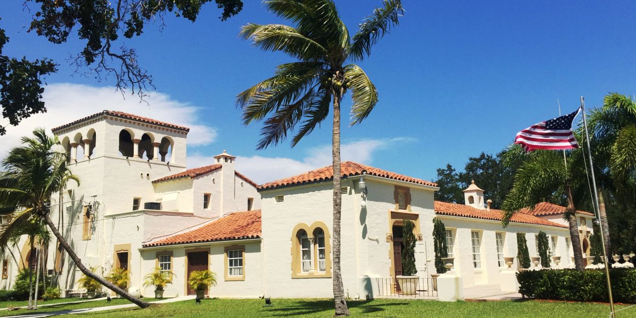 Mediterranean-style building with an American flag and palm trees.