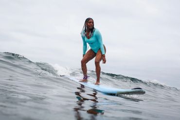 A woman in a turquoise wetsuit surfing on a blue surfboard.